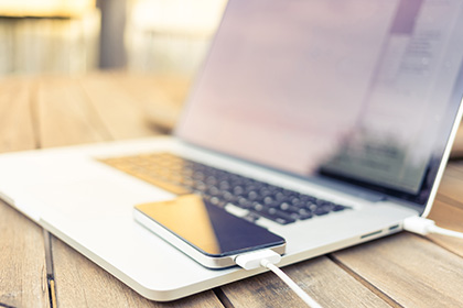 White cell phone connected to a white laptop