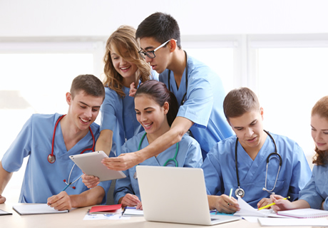 Six medical students sitting at a desk viewing a laptop and digital tablet